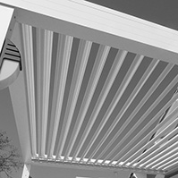 Pergola bioclimatique en alu à lames orientables et volets coulissants persiennés ouverts<br />