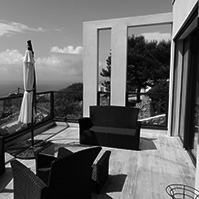 Terrasse façade Sud avec sièges en osier, barrières en verre et vue sur la mer<br />